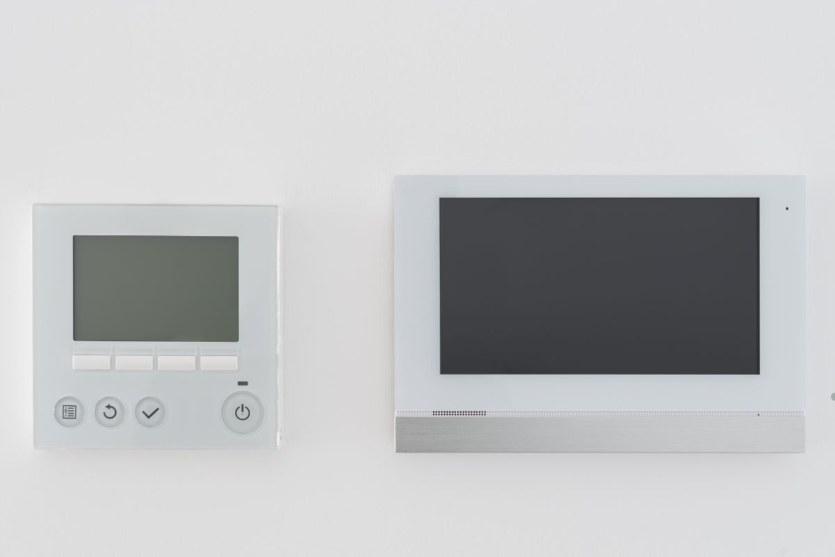 A white wall featuring a monitor, television, and clock, highlighting a home security video doorbell setup.
