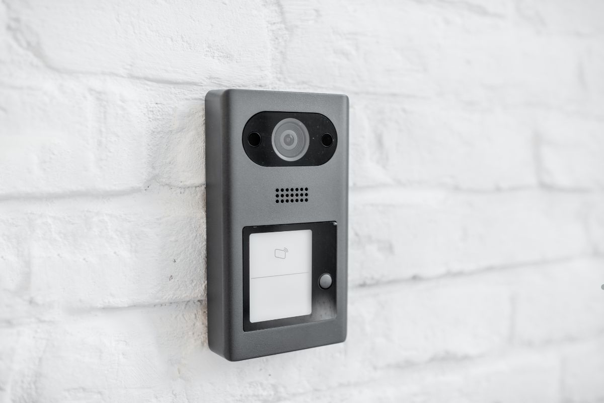 A video doorbell installed on a white brick wall, featuring a sleek design and a camera lens visible at the center.