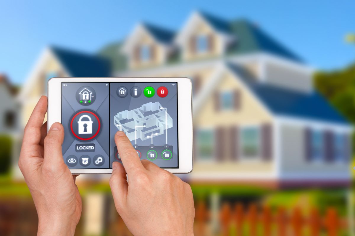 Hands holding a tablet displaying a home security system, with a house and security features visible in the background.